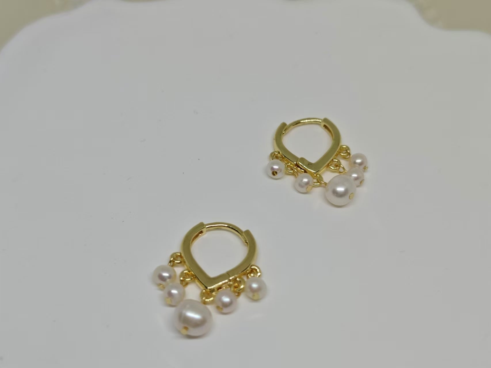 Two gold hoop earrings with five freshwater pearls each are displayed on a white surface.