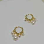 Two gold hoop earrings with five freshwater pearls each are displayed on a white surface.
