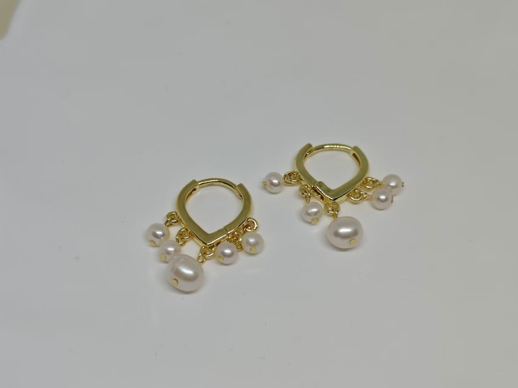 Two gold hoop earrings, each with five dangling freshwater pearls, are displayed on a white surface.