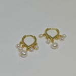 Two gold hoop earrings, each with five dangling freshwater pearls, are displayed on a white surface.