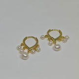 Two gold hoop earrings, each with five dangling freshwater pearls, are displayed on a white surface.