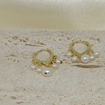 Gold hoop earrings with five dangling freshwater pearls on a textured light surface.