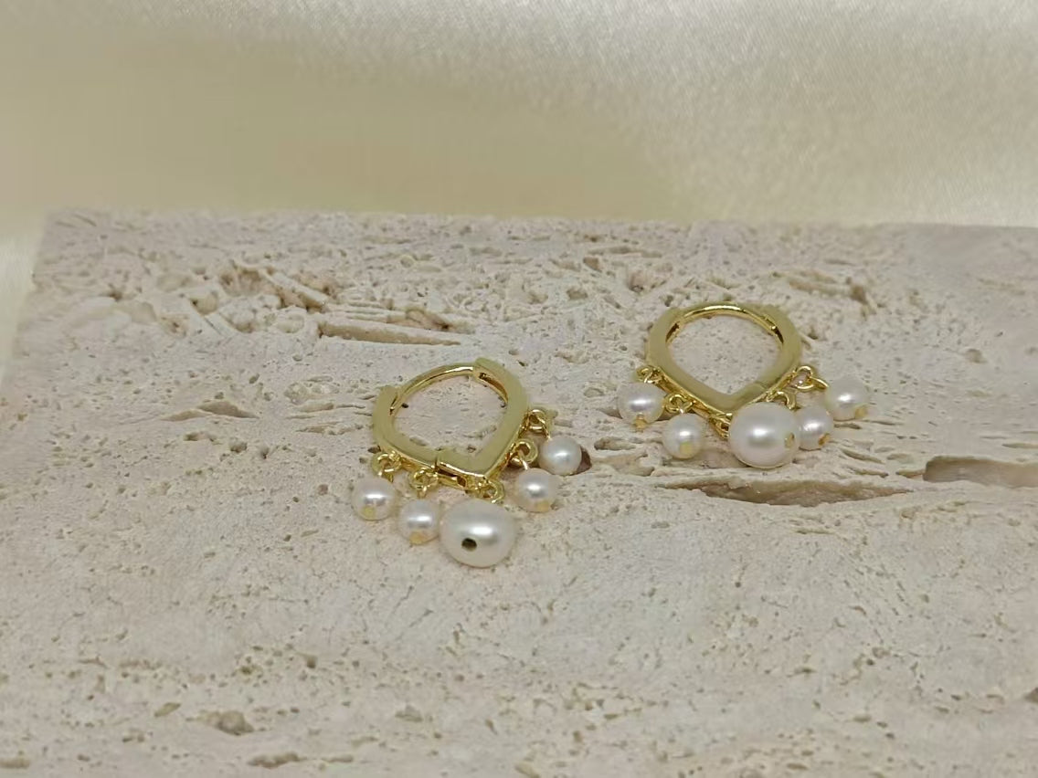 Gold hoop earrings with five dangling freshwater pearls on a textured light surface.