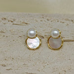 Two gold-framed earrings, each with a white pearl above a mother-of-pearl disc.