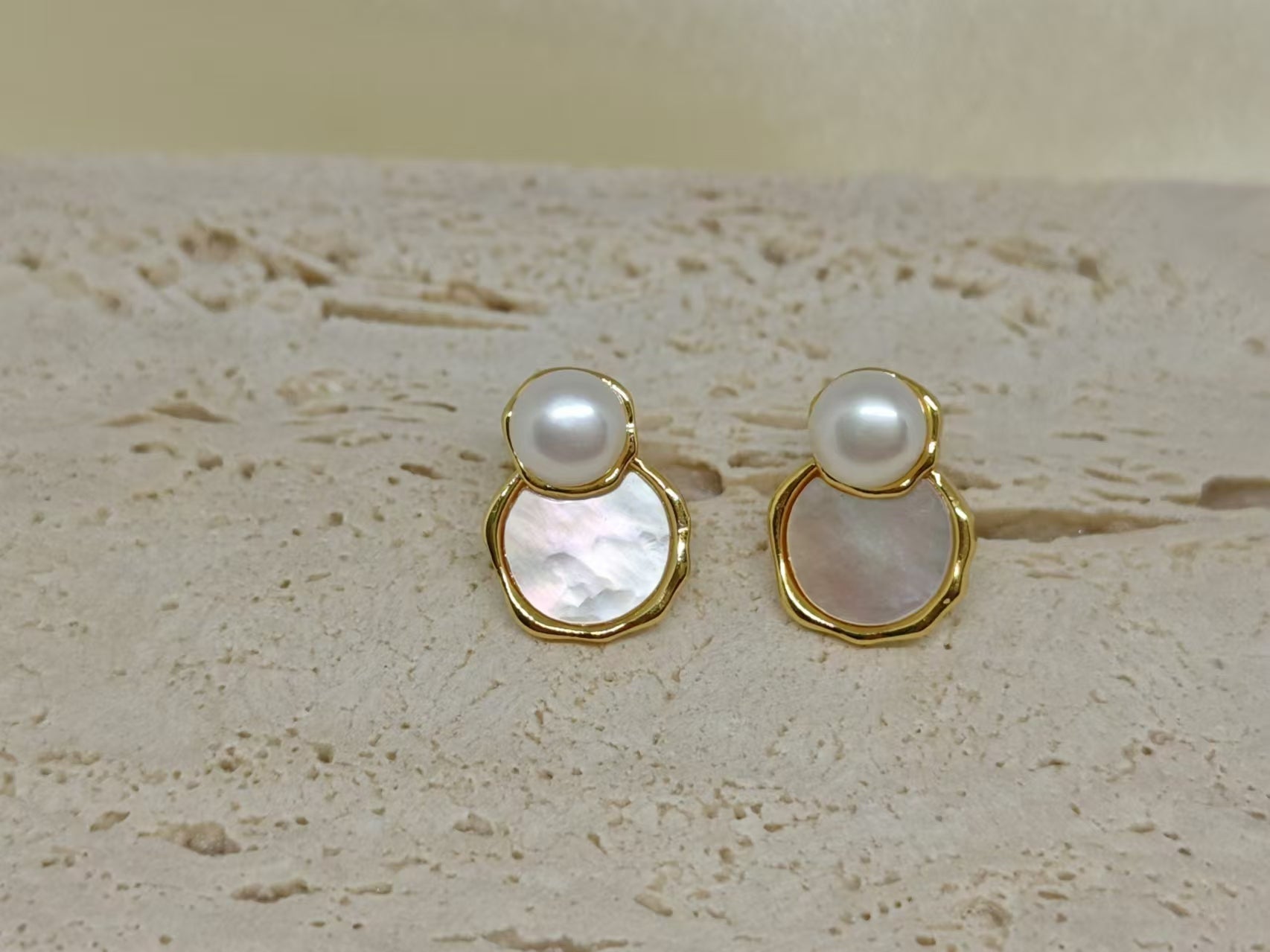 Two gold-framed earrings, each with a white pearl above a mother-of-pearl disc.