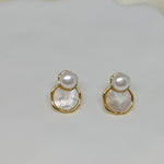 Two gold-framed earrings with a white pearl atop a mother-of-pearl disc.