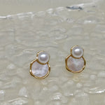 Two gold-rimmed earrings, each with a white pearl atop a mother-of-pearl disc.