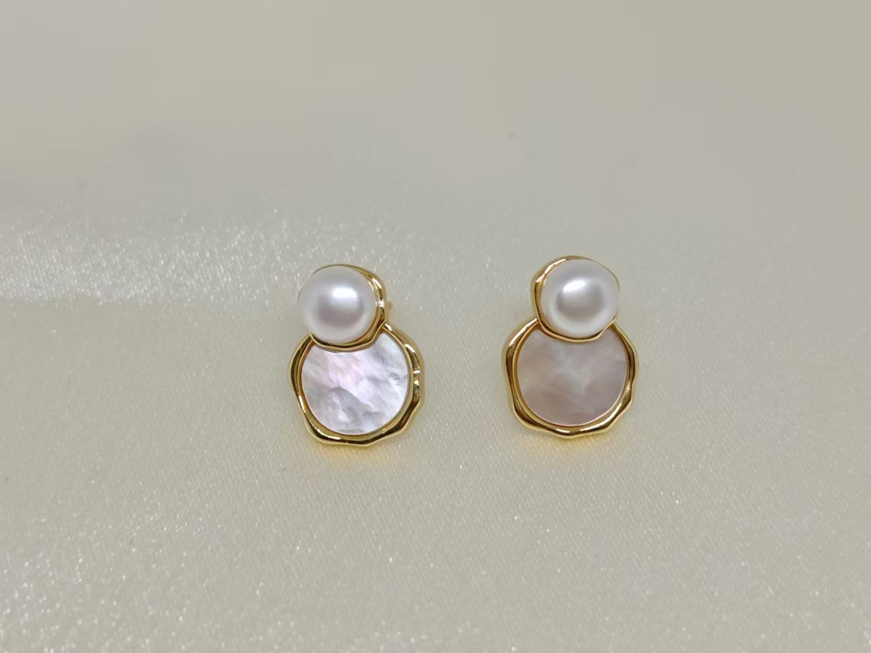 Two gold-framed earrings, each with a white pearl atop a mother-of-pearl disc.
