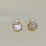Two gold-framed earrings, each with a white pearl atop a mother-of-pearl disc.