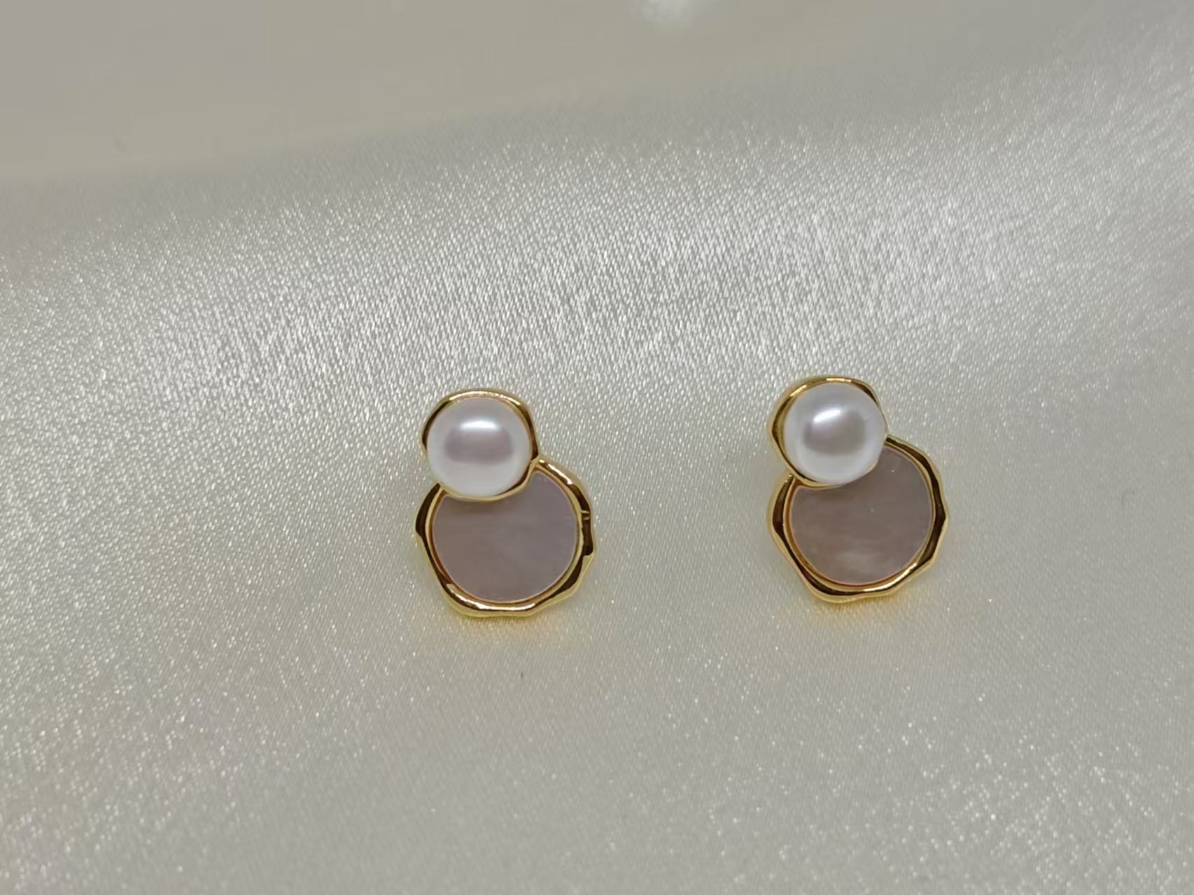 Gold-toned earrings with a white pearl atop a light pink, irregular-shaped stone.