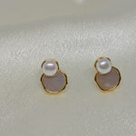 Gold-toned earrings with a white pearl atop a light pink, irregular-shaped stone.