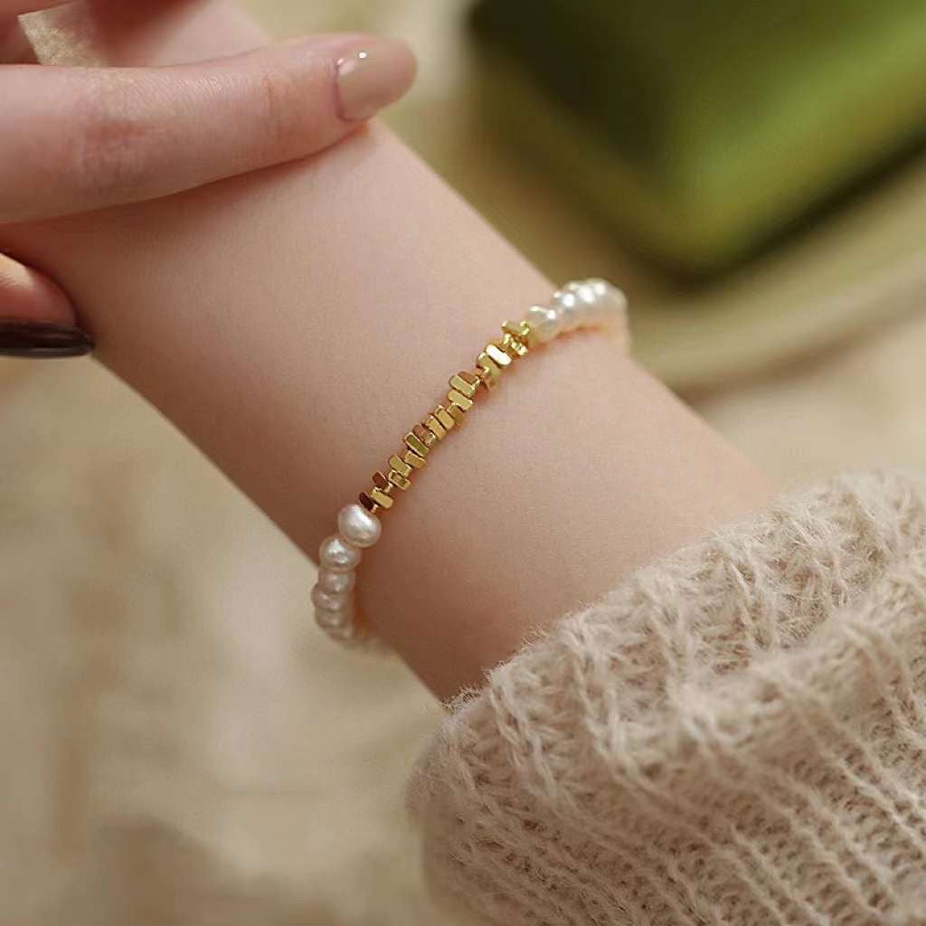 A woman's arm wears a freshwater pearl bracelet with gold rectangular beads.