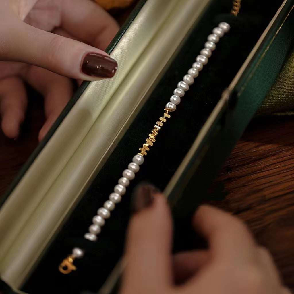 A person holds open a dark green velvet box revealing a freshwater pearl bracelet.