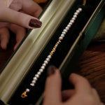 A person holds open a dark green velvet box revealing a freshwater pearl bracelet.