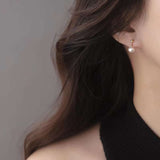 A woman wears a small pearl dangle earring with a gold stud.