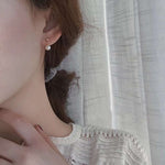 A woman wears a small pearl dangle earring with a gold-plated stud.