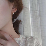 A woman wears a small pearl dangle earring with a gold-plated stud.