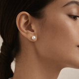 A single pearl stud earring is shown on a woman's ear.