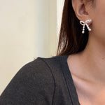 A woman wears a butterfly bow stud earring crafted from small, luminous white pearls.