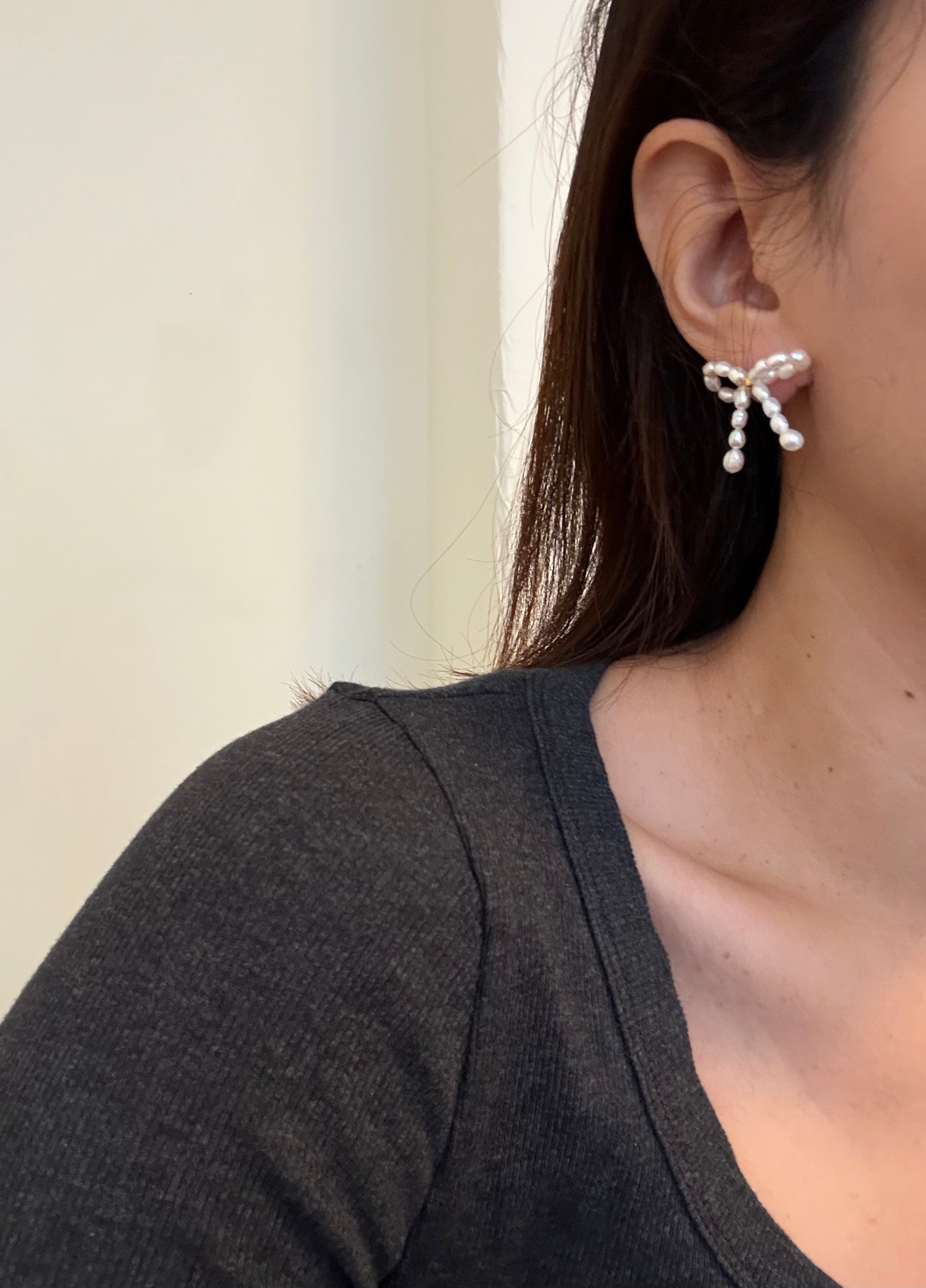 A woman wears a butterfly bow stud earring crafted from small, luminous white pearls.