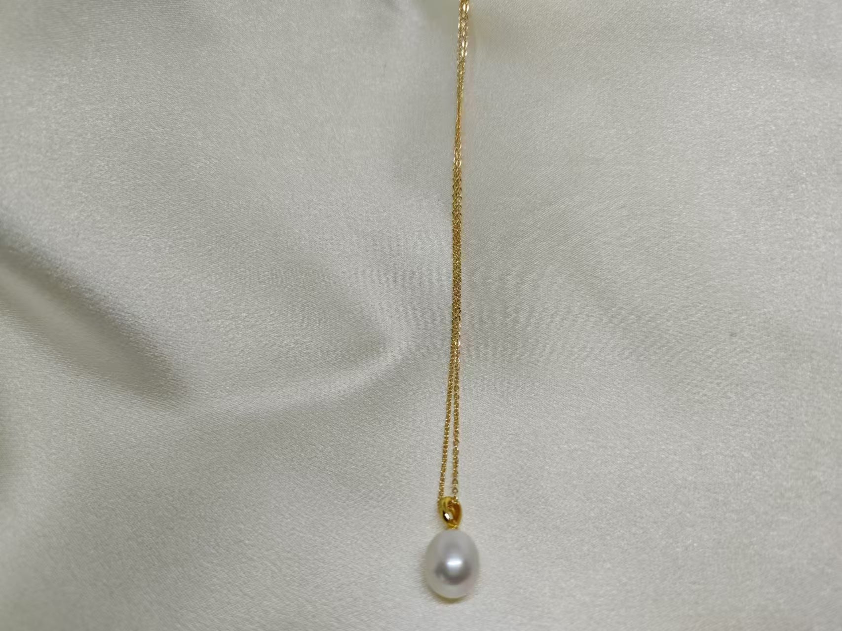 A white freshwater pearl necklace with a gold chain on a light-colored fabric background.