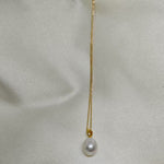 A white freshwater pearl necklace with a gold chain on a light-colored fabric background.