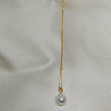 A white freshwater pearl necklace with a gold chain on a light-colored fabric background.