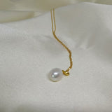 A white, off-round freshwater pearl hangs from a delicate gold chain on a white fabric.