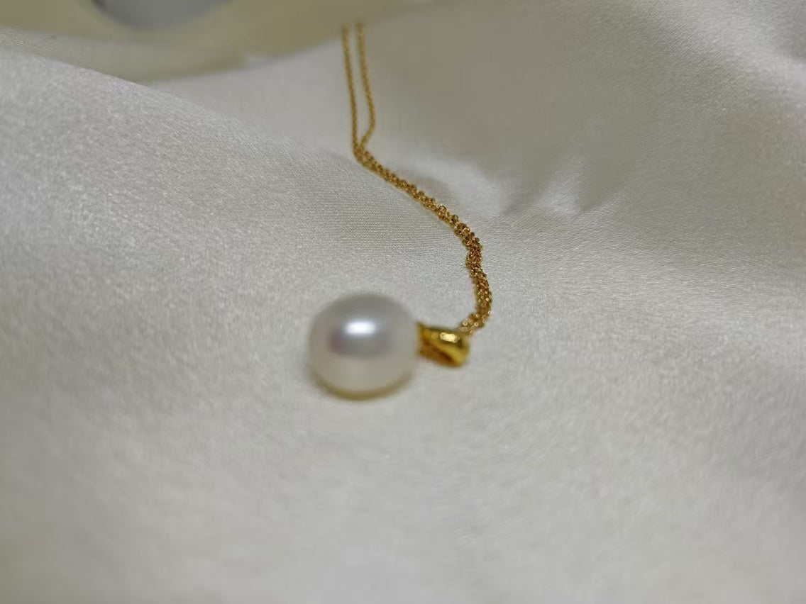 White freshwater pearl necklace with a gold chain on a white fabric background.