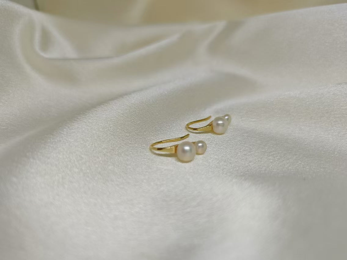 Gold-plated freshwater pearl stud earrings with curved hooks on white fabric.