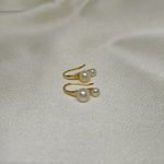 Gold-plated freshwater pearl stud earrings with curved hooks on a white fabric background.