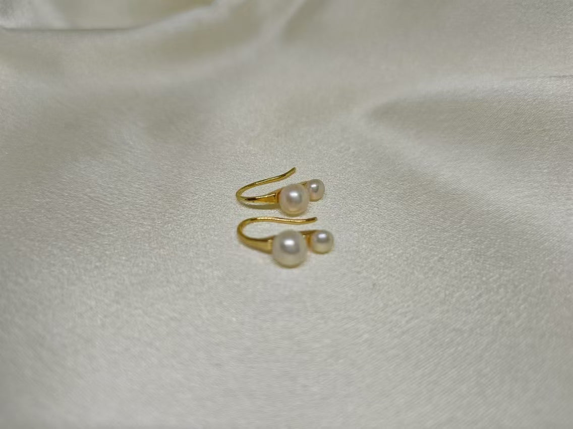 Gold-plated freshwater pearl stud earrings with curved hooks on a white fabric background.