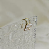Gold-plated freshwater pearl stud earrings with curved hooks on a textured clear surface.