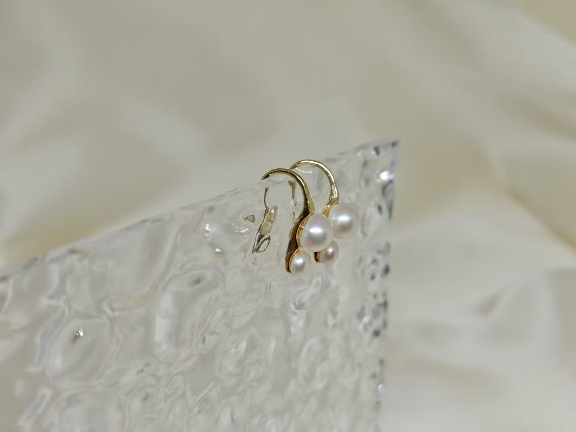 Gold-plated freshwater pearl stud earrings with curved hooks on a textured clear surface.