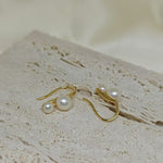 Gold-plated freshwater pearl stud earrings with curved hooks on a textured surface.