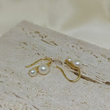 Gold-plated freshwater pearl stud earrings with curved hooks on a textured surface.