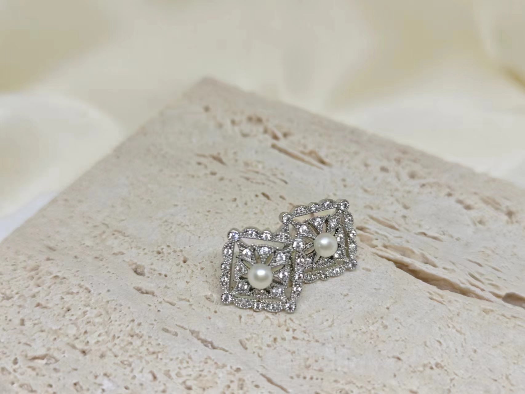 Silver quadrate stud earrings with a central freshwater pearl and surrounding small diamonds.