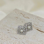 Silver quadrate stud earrings with a central freshwater pearl and surrounding small diamonds.