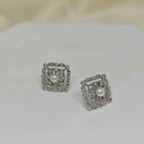 A pair of silver square stud earrings with a central pearl surrounded by small diamonds.