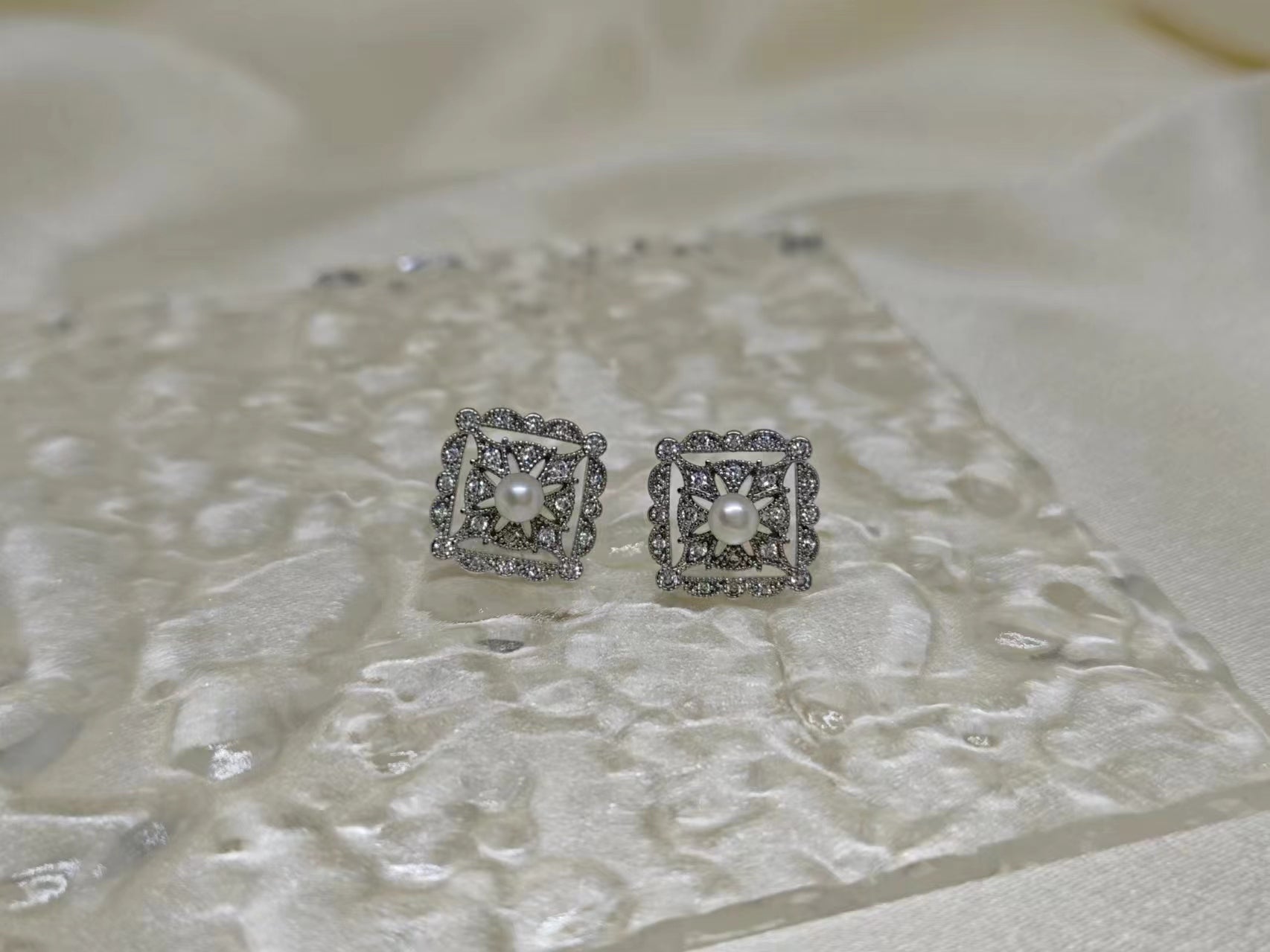 Silver quadrate vintage stud earrings with a central freshwater pearl and surrounding diamonds.