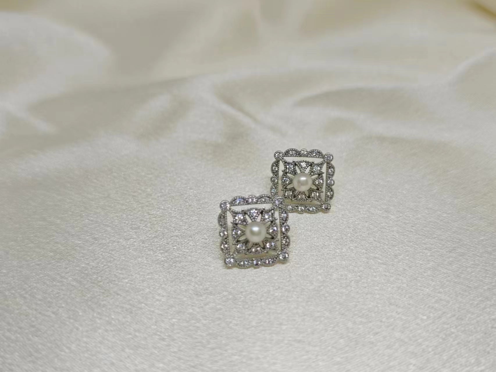 Silver quadrate stud earrings with a central pearl surrounded by small diamonds.