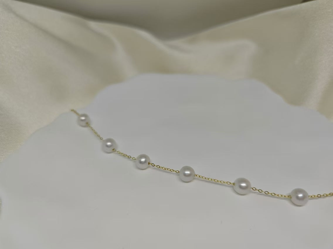 A delicate gold chain bracelet features seven evenly spaced white freshwater pearls.