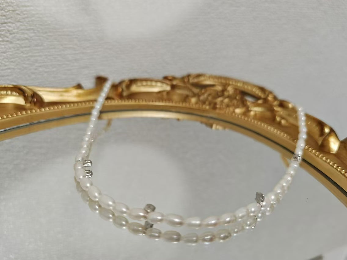 A two-strand freshwater pearl necklace with silver accents rests on a mirrored surface.