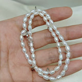 A double-wrapped freshwater pearl bracelet is held in a person's hand.