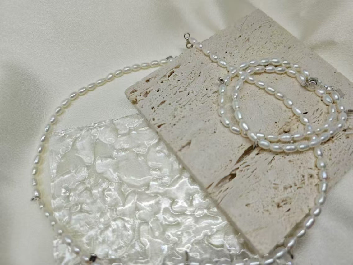 A double-wrapped freshwater pearl bracelet is displayed on a textured stone surface.