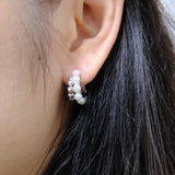 A woman wears a silver half-ring earring with pearls on her right ear.