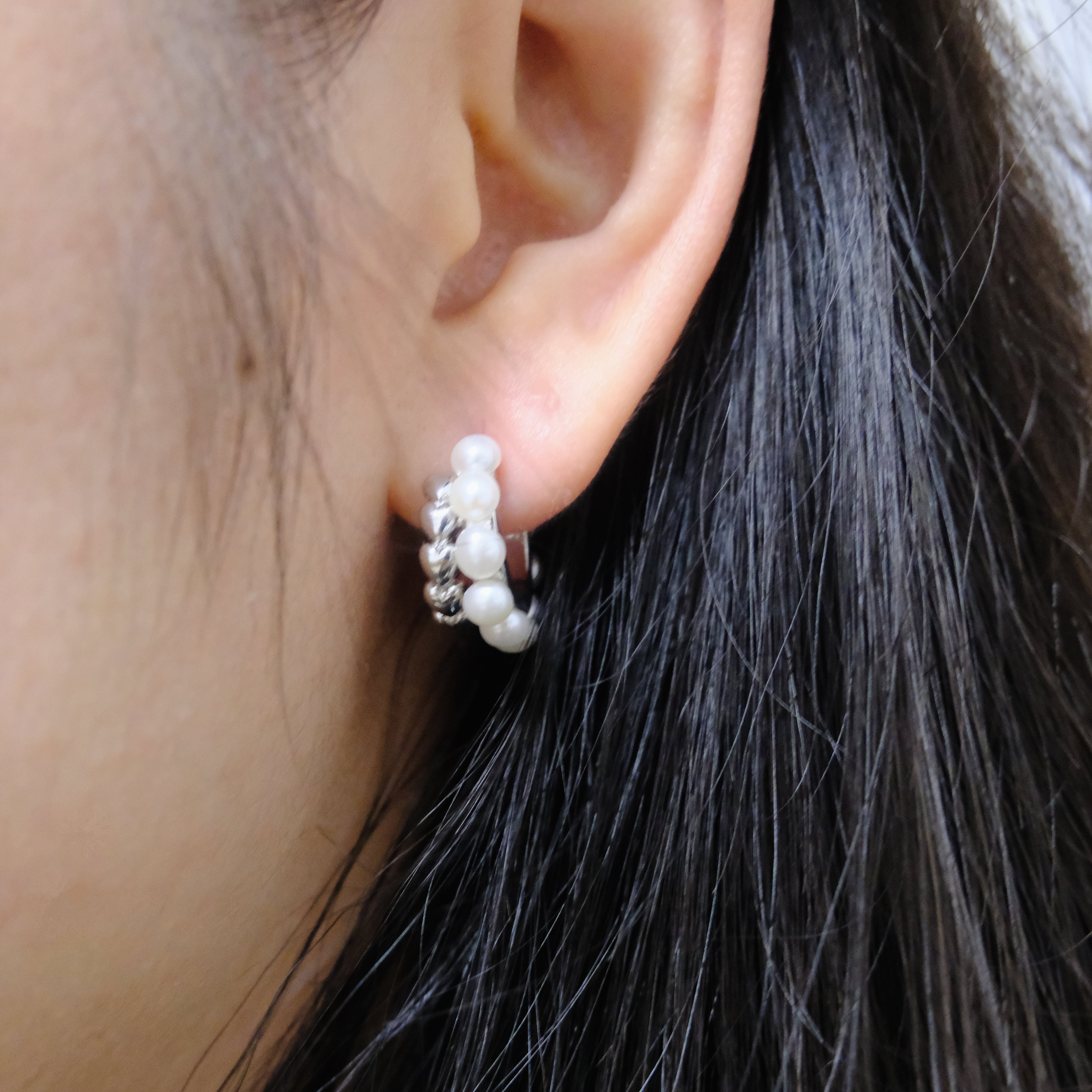 A woman wears a silver half-ring earring with pearls on her right ear.