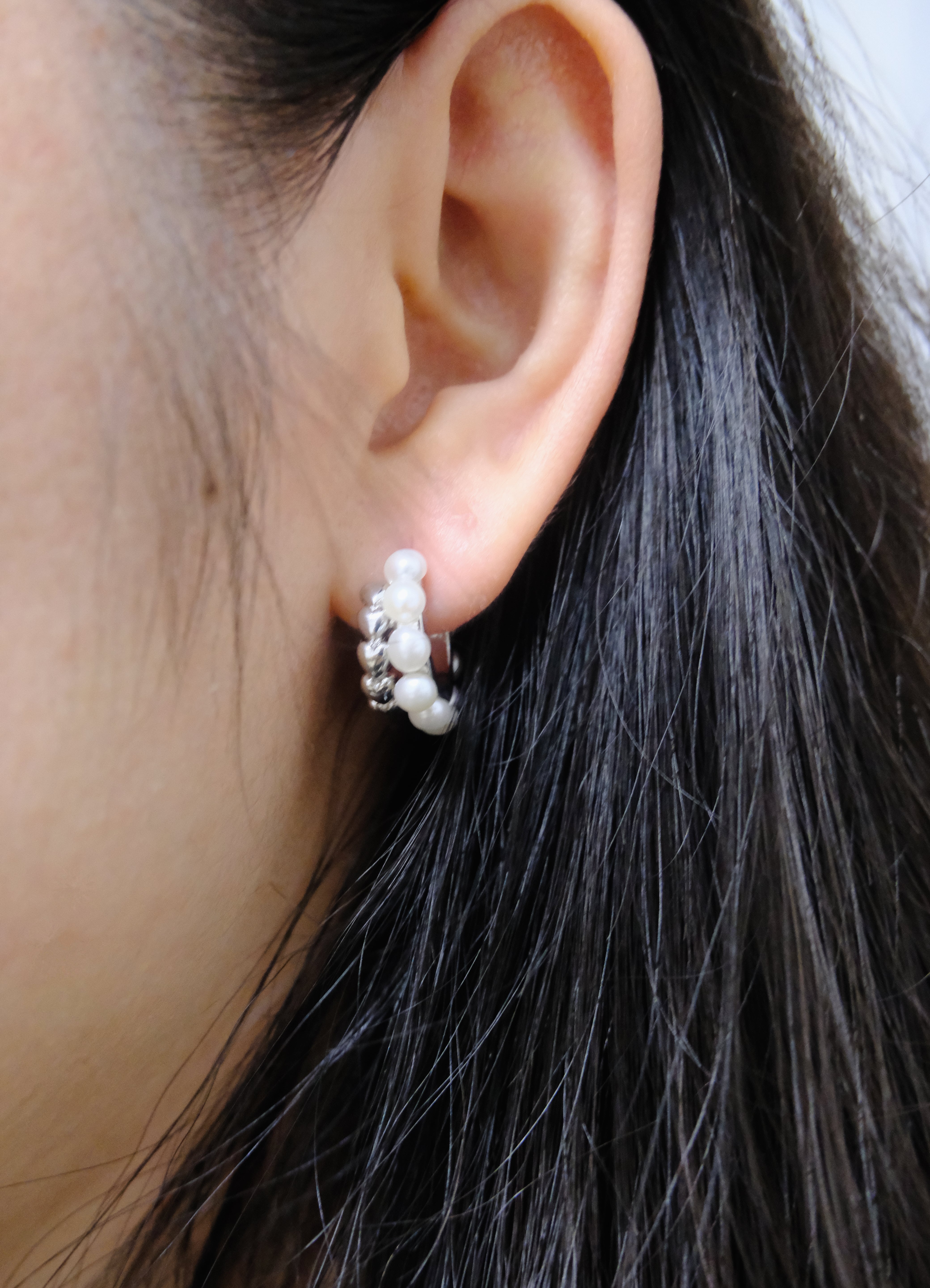 A woman wears a silver half-ring earring with pearls on her right ear.