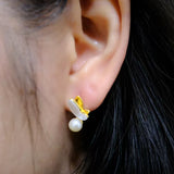 A gold-plated butterfly stud earring with a freshwater pearl dangles from an ear.