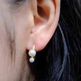 Gold-plated freshwater pearl stud earrings with curved hooks on an ear.